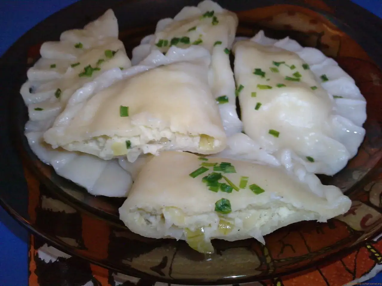 Pyszne pierogi ruskie przepis babci, z serem i ziemniakami, posypane szczypiorkiem.