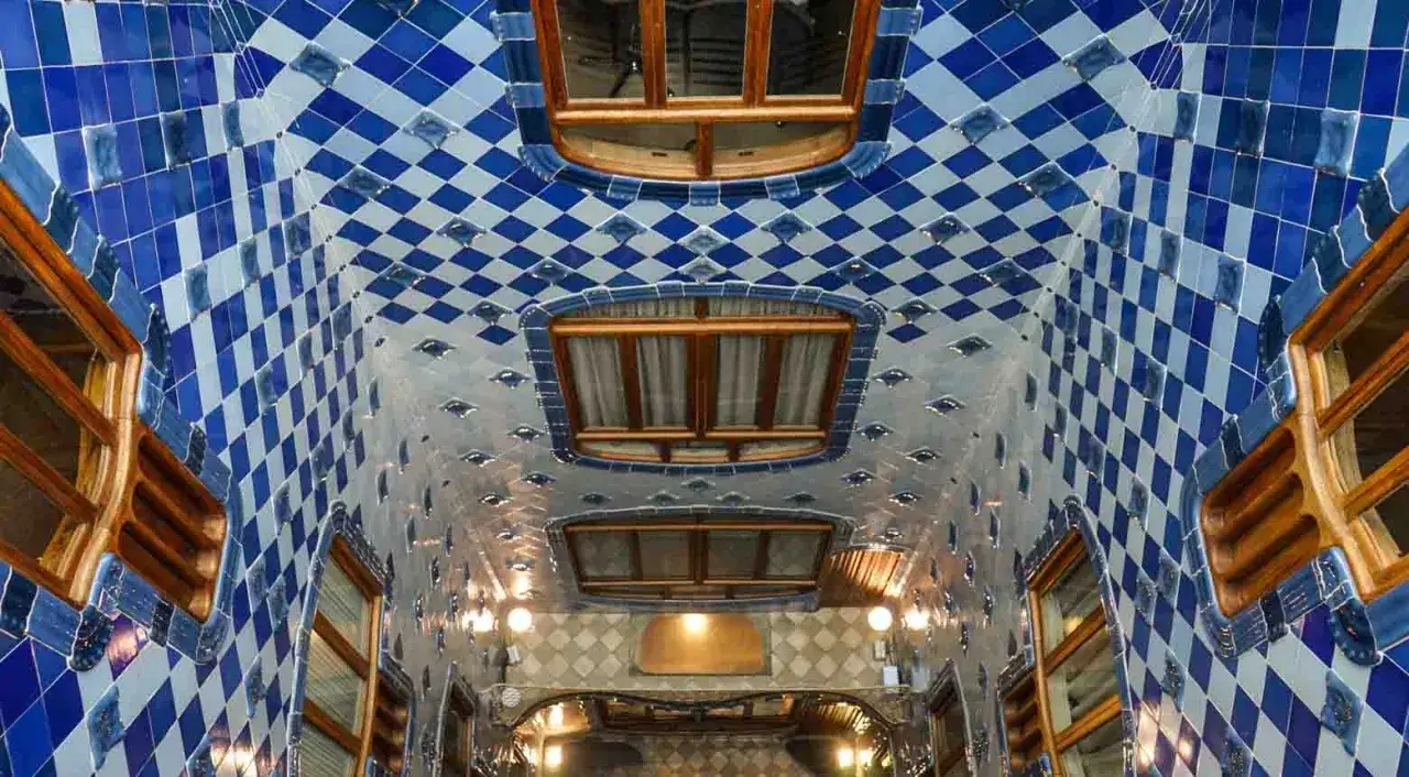 Interno della Casa Batll&oacute;: soffitto ondulato con piastrelle blu e bianche a rombi, finestre in legno e luci soffuse.