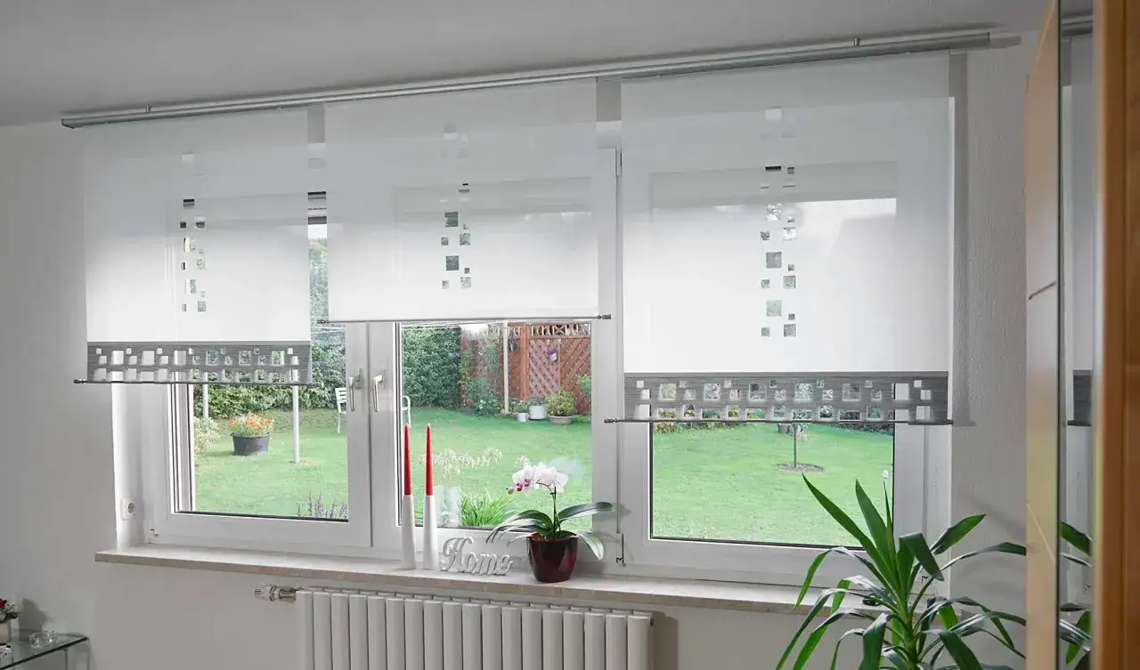 Moderne Gardinen bis zur Fensterbank mit quadratischem Muster, die den Blick auf einen grünen Garten freigeben.