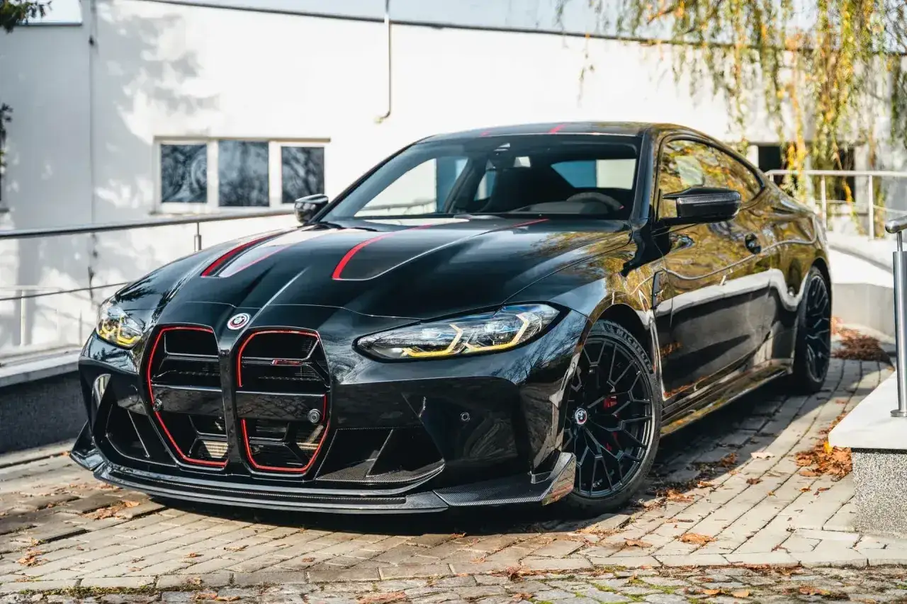 Czarny BMW M4 CSL z czerwonymi akcentami, gotowy do jazdy po jesiennych liściach.