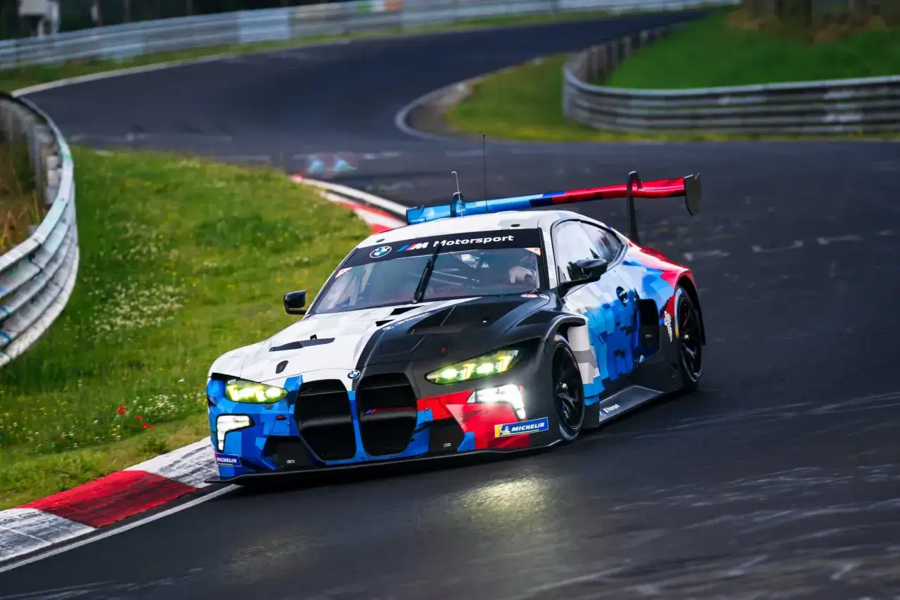 Ein BMW M4 GT3 rast &uuml;ber die Rennstrecke, seine Scheinwerfer leuchten hell.