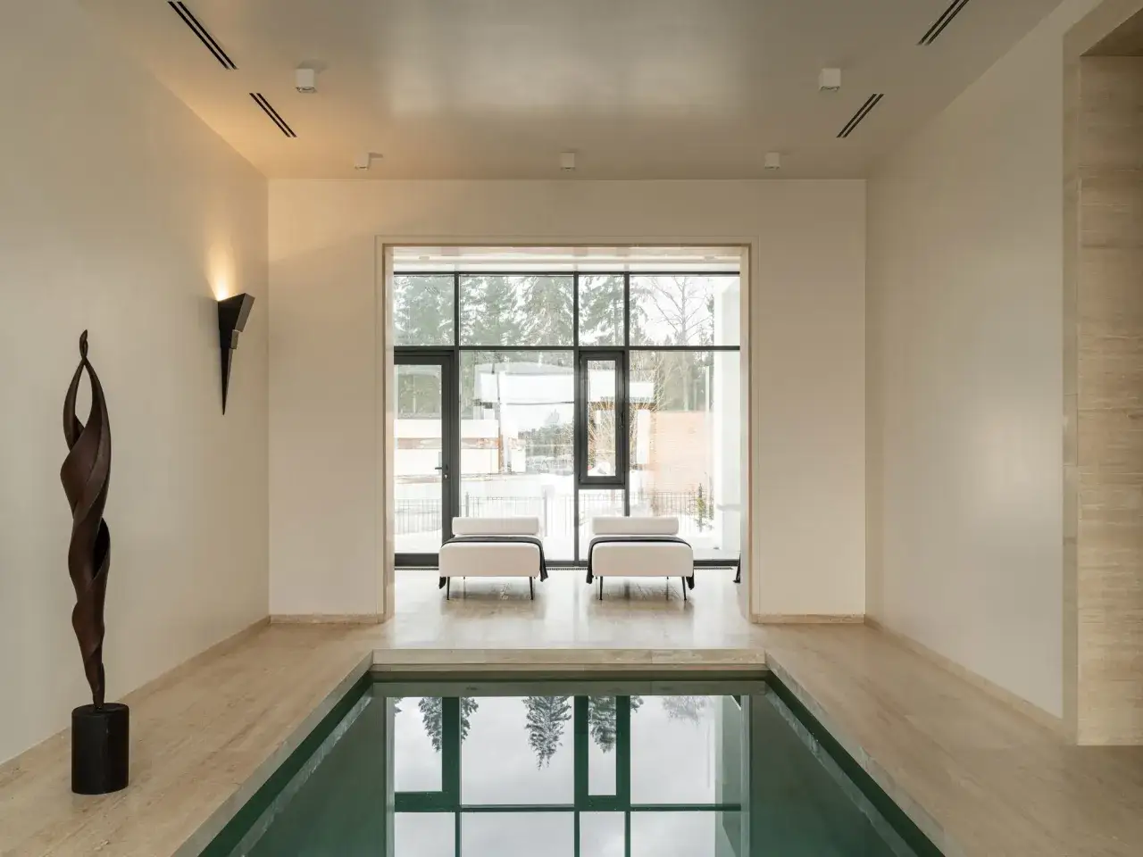 Relajante espacio con piscinas interiores, tumbonas blancas y una escultura de madera.