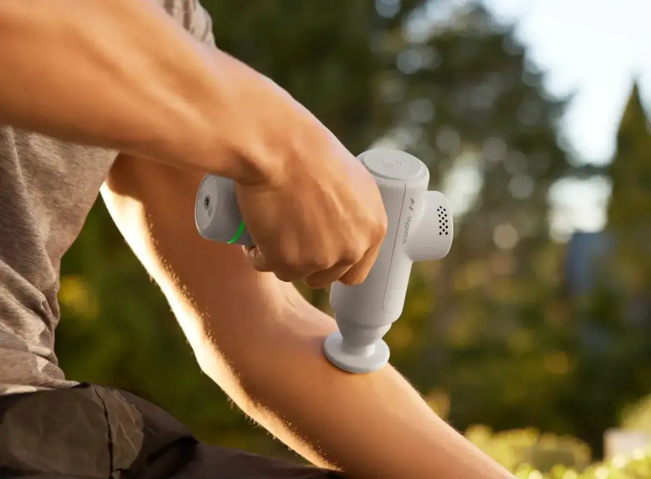 A person uses a handheld massager on their arm, showing how handheld massagers work for muscle recovery.