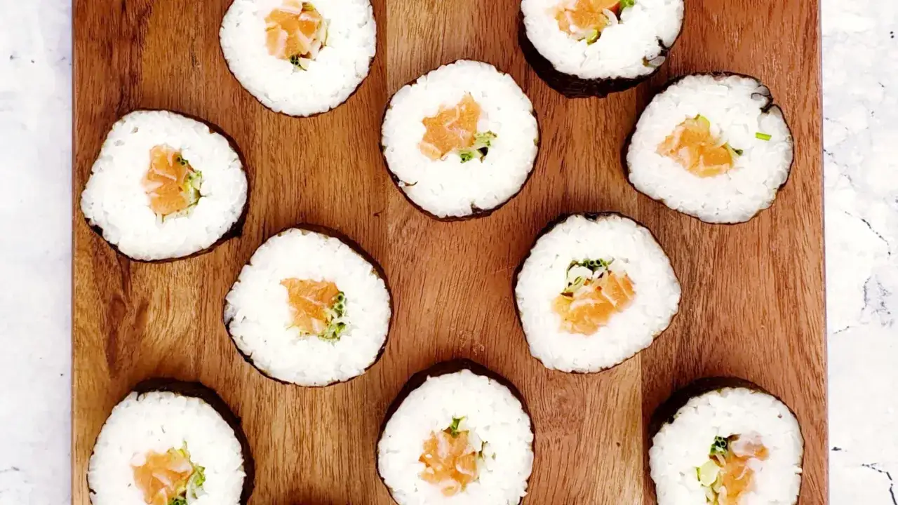 Diez rollos de maki sushi con salm&oacute;n y aguacate, dispuestos sobre una tabla de madera.