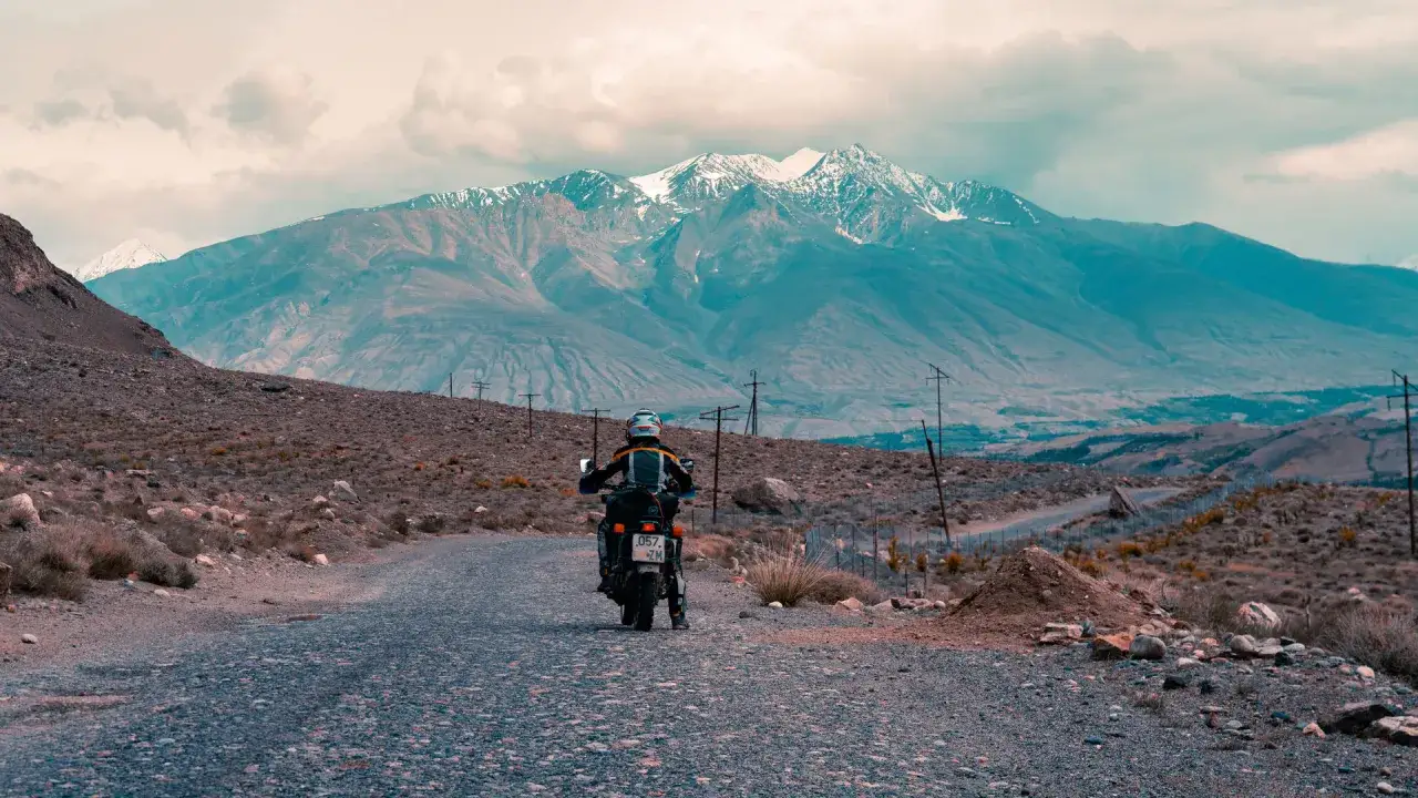 Motocyklista przemierza pustynny krajobraz u podnóża majestatycznych gór Pamir.