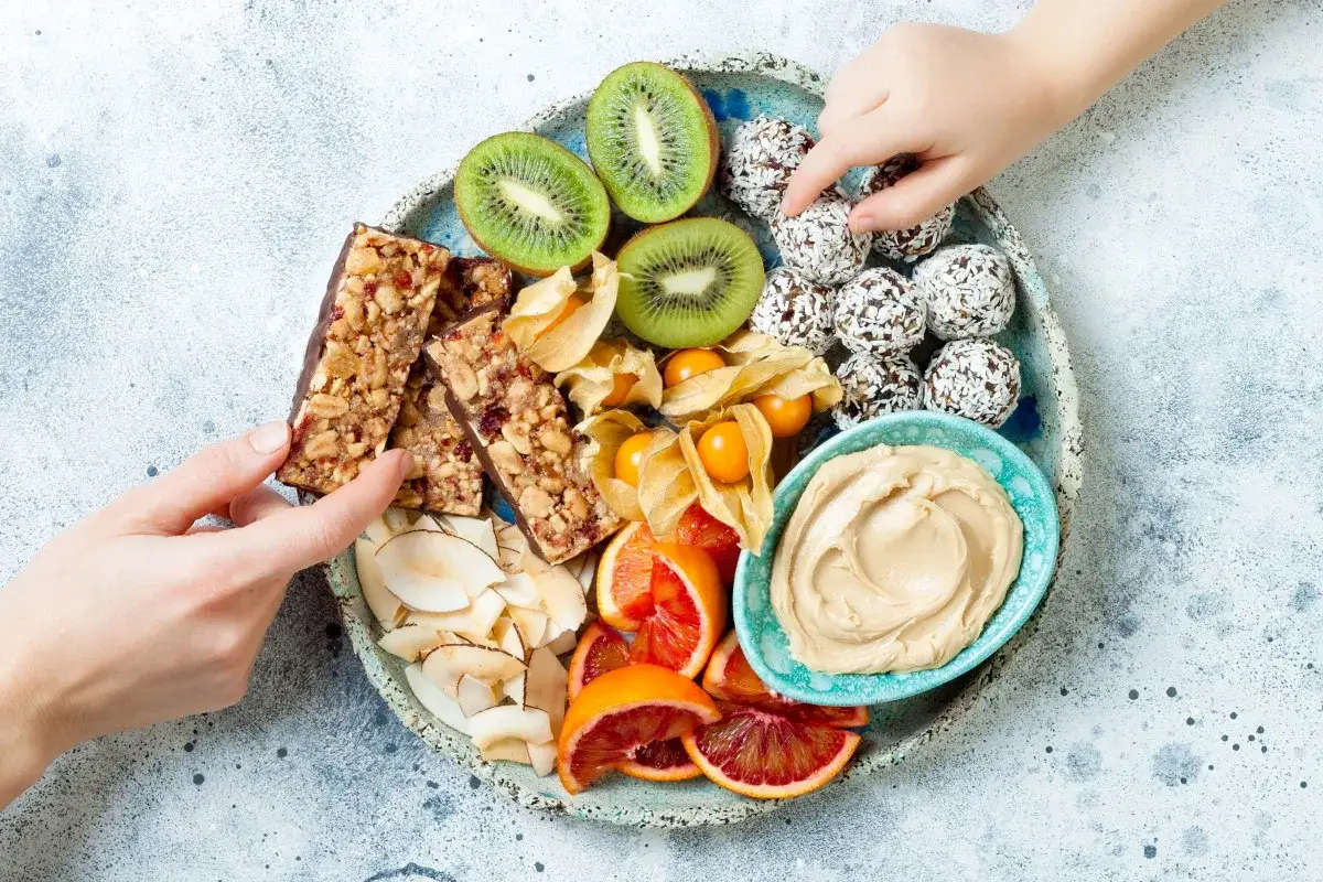 Na talerzu pełnym pyszności: batony, kiwi, daktyle w wiórkach, pomarańcze, physalis i masło orzechowe. Idealne owoce na noc.