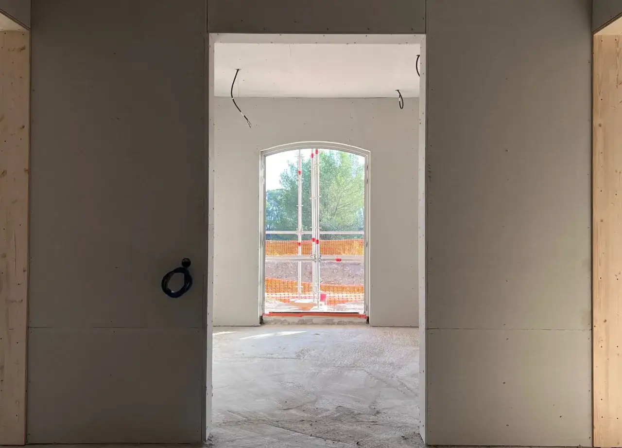 Intérieur en cours de finition, murs en fermacell ou placo, avec une fenêtre cintrée donnant sur l'extérieur.