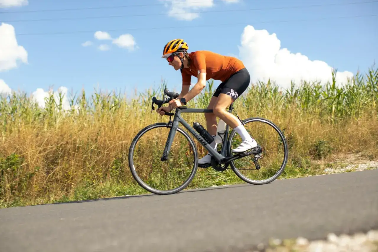 A cyclist enjoys a solo ride on a sunny day, perhaps a vuelta rest day, with a field of tall grass beside the road.
