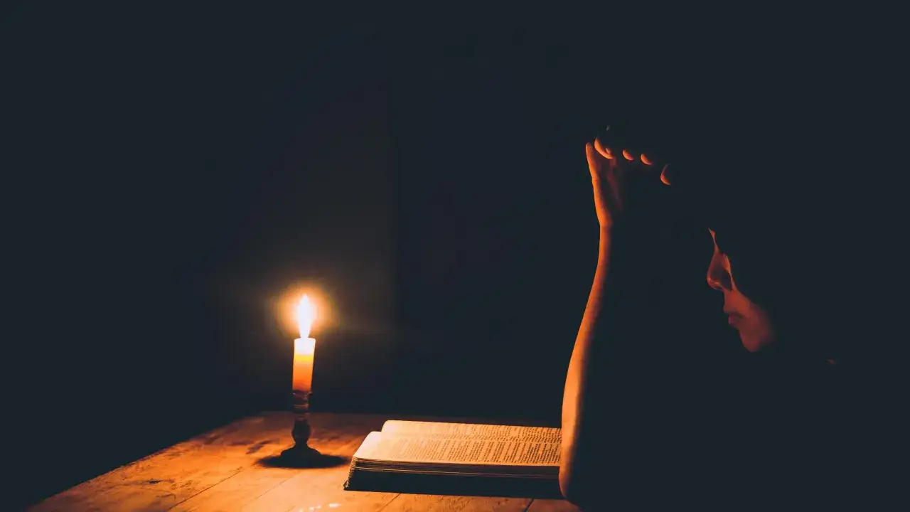 A person reads a book by candlelight, seeking guidance through 7 prayers for obedience to God.