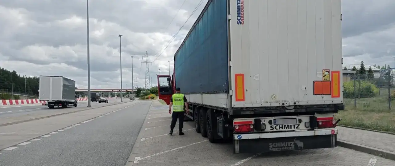 Inspektor w kamizelce odblaskowej dokonuje sprawdzenia licencji transportowej przy zaparkowanej ciężarówce.