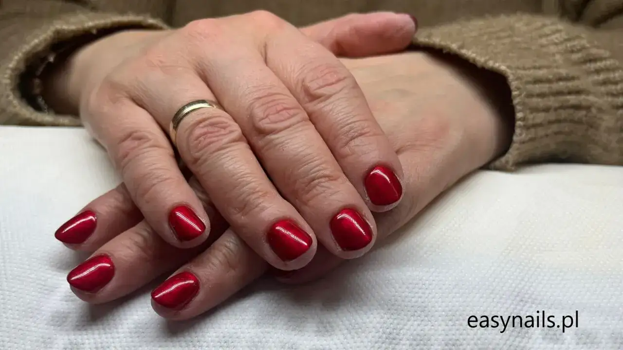 Dłonie kobiety z pokolenia babyboomer z eleganckim, czerwonym manicure. Złoty pierścionek dodaje klasy.