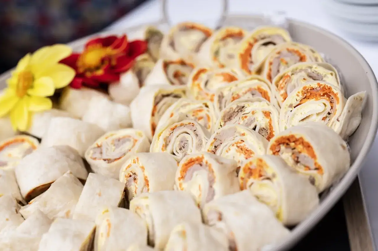 Plateau de wraps froids coupés en tronçons, garniture visible de viande et carottes râpées. Parfait pour une recette wrap froid.