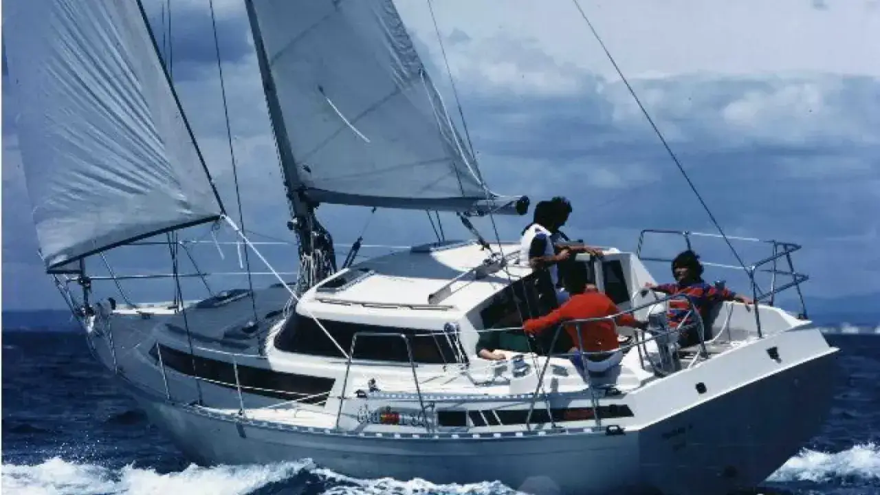 Voile blanche gonflée, quatre personnes sur un voilier blanc naviguant sur une mer agitée. L'évasion 34 avis semble être un bon choix pour cette aventure.