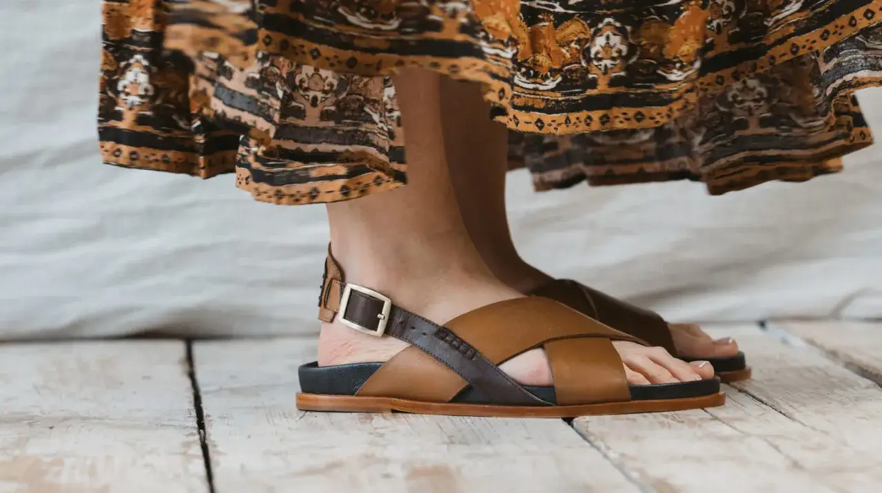 Orteils qui dépassent des sandales en cuir marron, sous une robe bohème.
