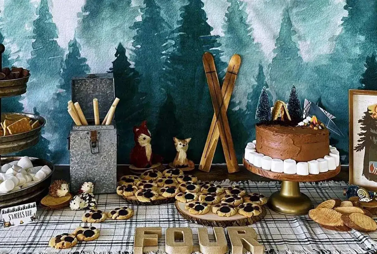 A woodland-themed dessert table with a chocolate cake, cookies, and s'mores supplies, perfect for camping birthday ideas.