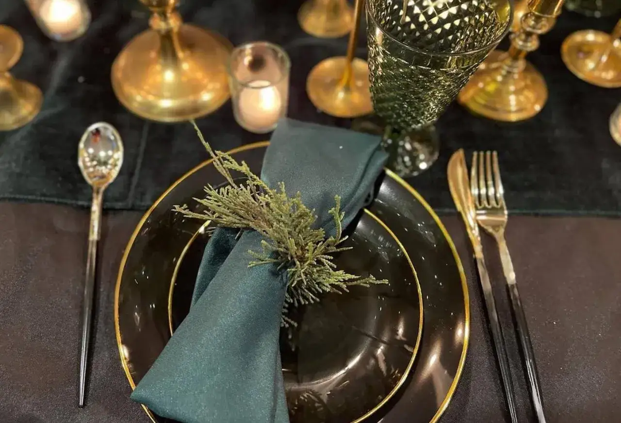 Elegant ny&aring;rsdukning med m&ouml;rkgr&ouml;na servetter, guldbestick och en grankvist. Vackert f&ouml;r en festlig kv&auml;ll.