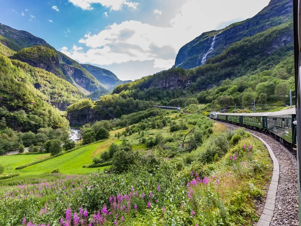 Zielony pociąg mknie przez norweski fiord, odkrywając jedne z najpiękniejszych tras kolejowych w Europie. Wodospad i kwitnące łąki towarzyszą podróży.