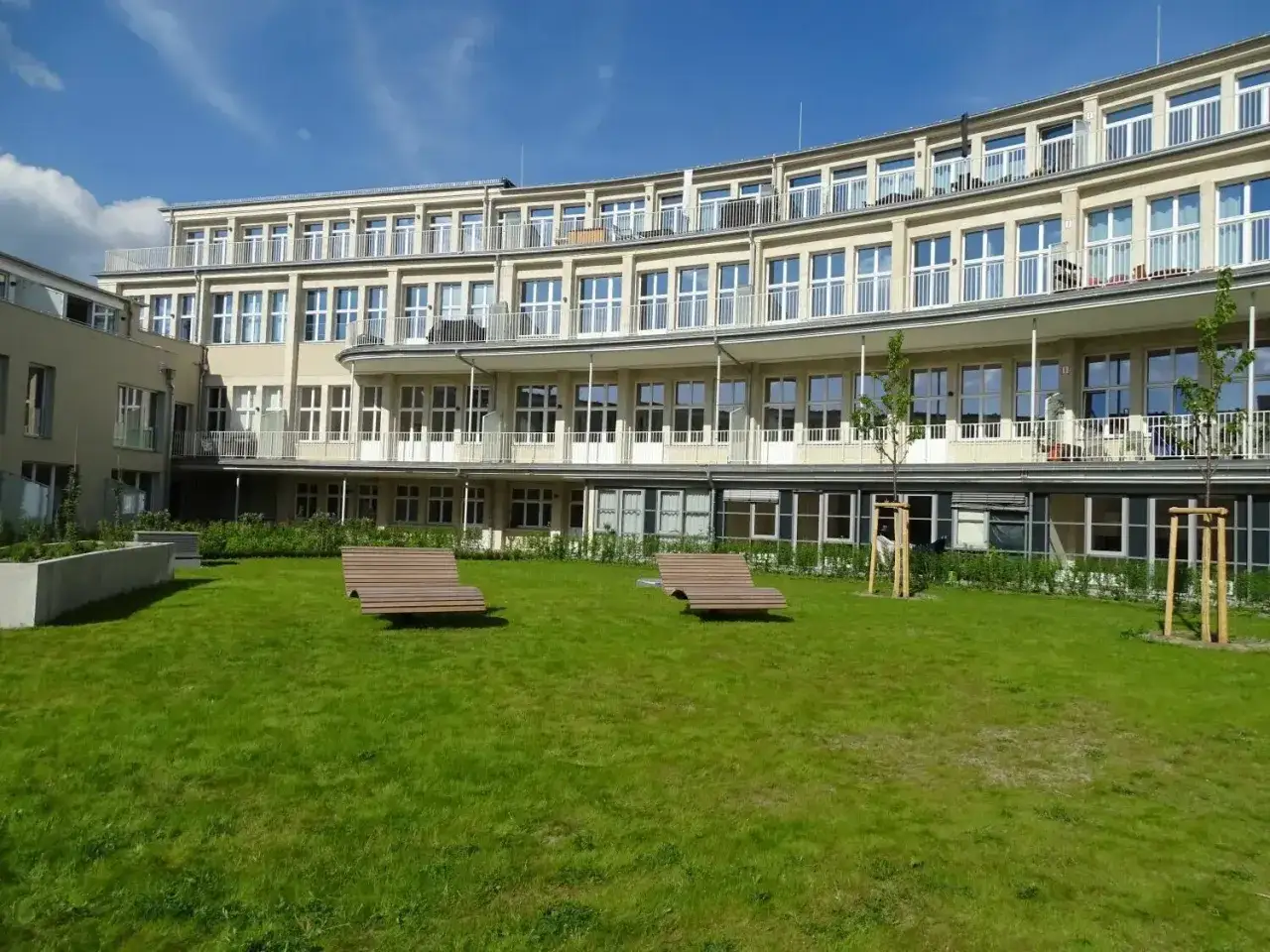 Gr&uuml;ne Rasenfl&auml;che mit zwei Holzliegen vor einem modernen Geb&auml;ude im olympisches Dorf Berlin.