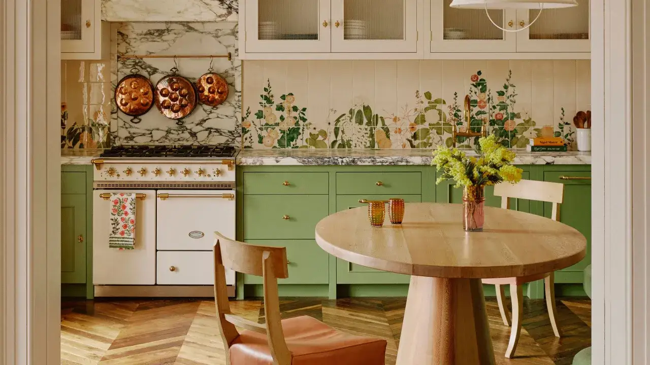 Cucina con mobili verdi, piano in marmo e piastrelle floreali. Un tavolo in legno con sedie e un mazzo di mimose. Perfetta per scoprire le cose da fare a Roma nel weekend.