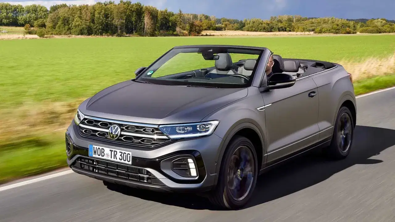 Szary Volkswagen T-Roc Cabrio z opuszczonym dachem jedzie po drodze wśród zielonych pól.