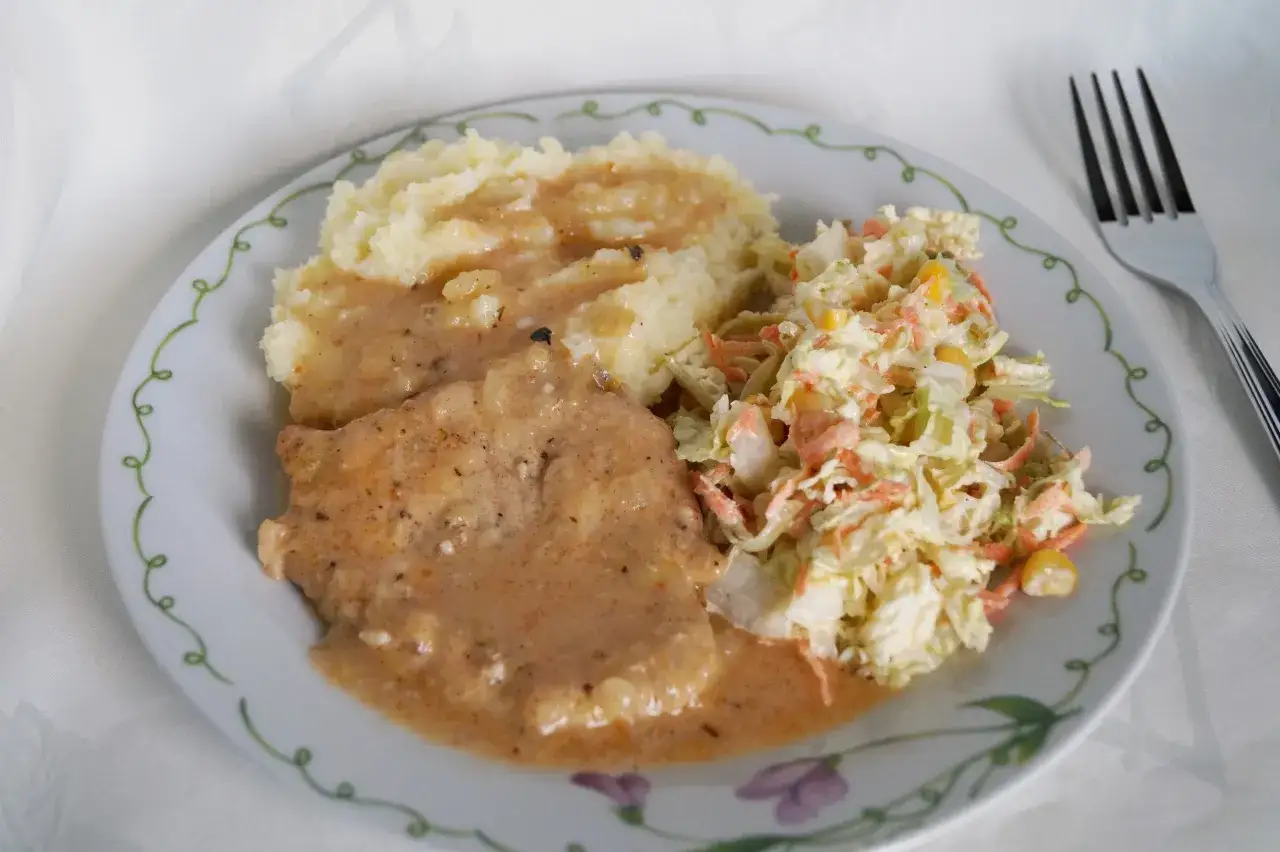 Pyszny schab w sosie podany z puree ziemniaczanym i surówką z kapusty.