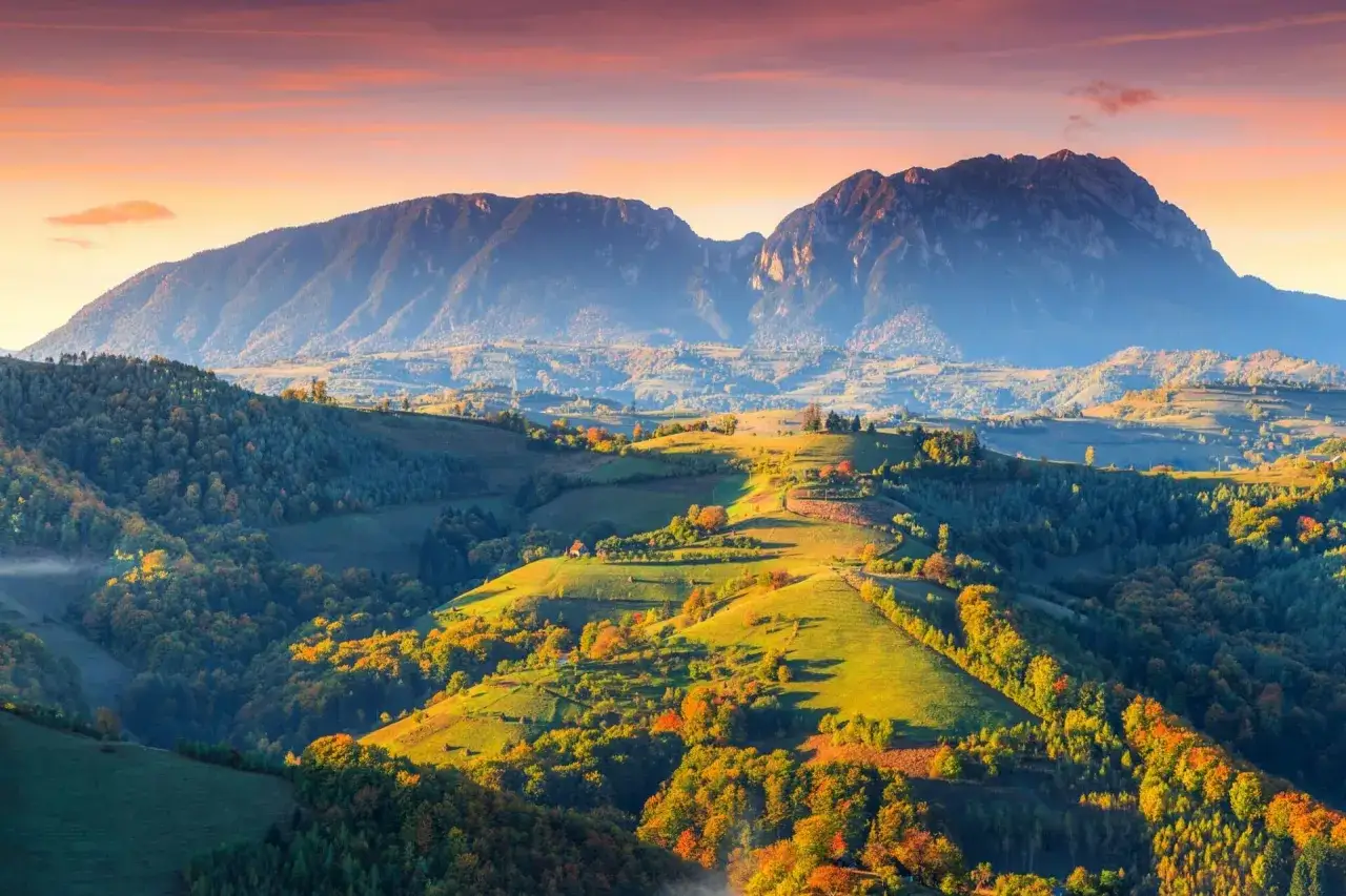 Paysages vallonnés et montagnes majestueuses au lever du soleil, une invitation à visiter la Roumanie.