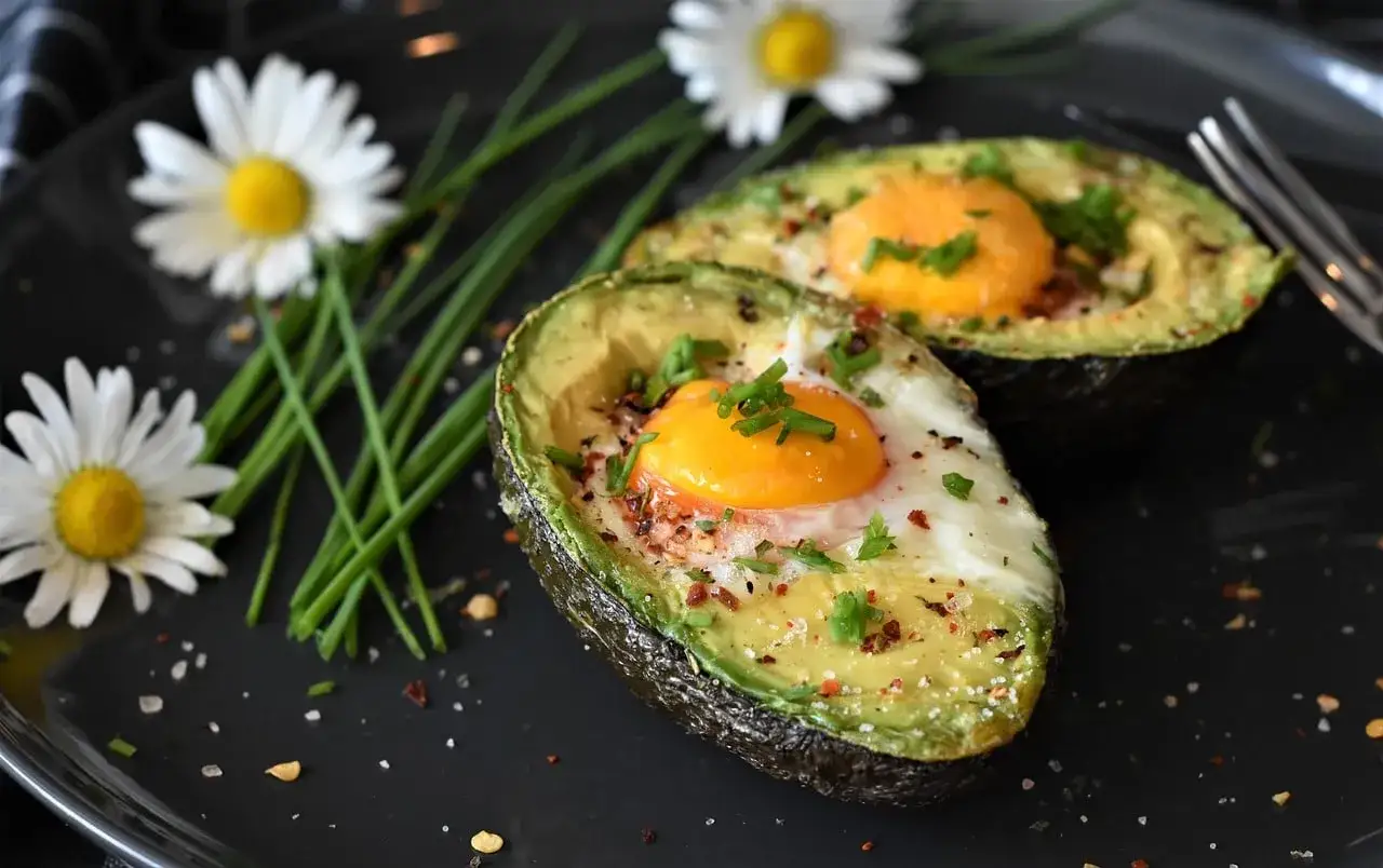 Deux moitiés d'avocat garnies d'un œuf au four, parsemées d'herbes et d'épices. Un plat sain et savoureux, parfait pour un brunch.
