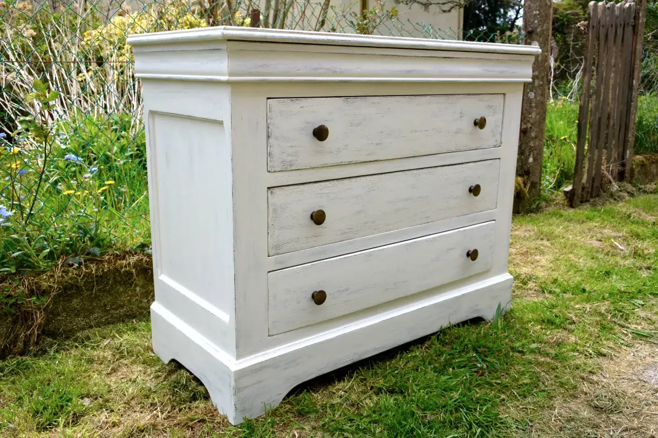 Commode ancienne repeinte en blanc patiné, prête à être customisée. Ses tiroirs aux poignées rondes en laiton attendent une nouvelle vie.