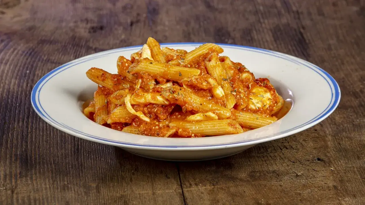 Piatto di pasta alla checca con pomodoro e mozzarella, servita su un piatto bianco con bordo blu, su un tavolo di legno rustico.