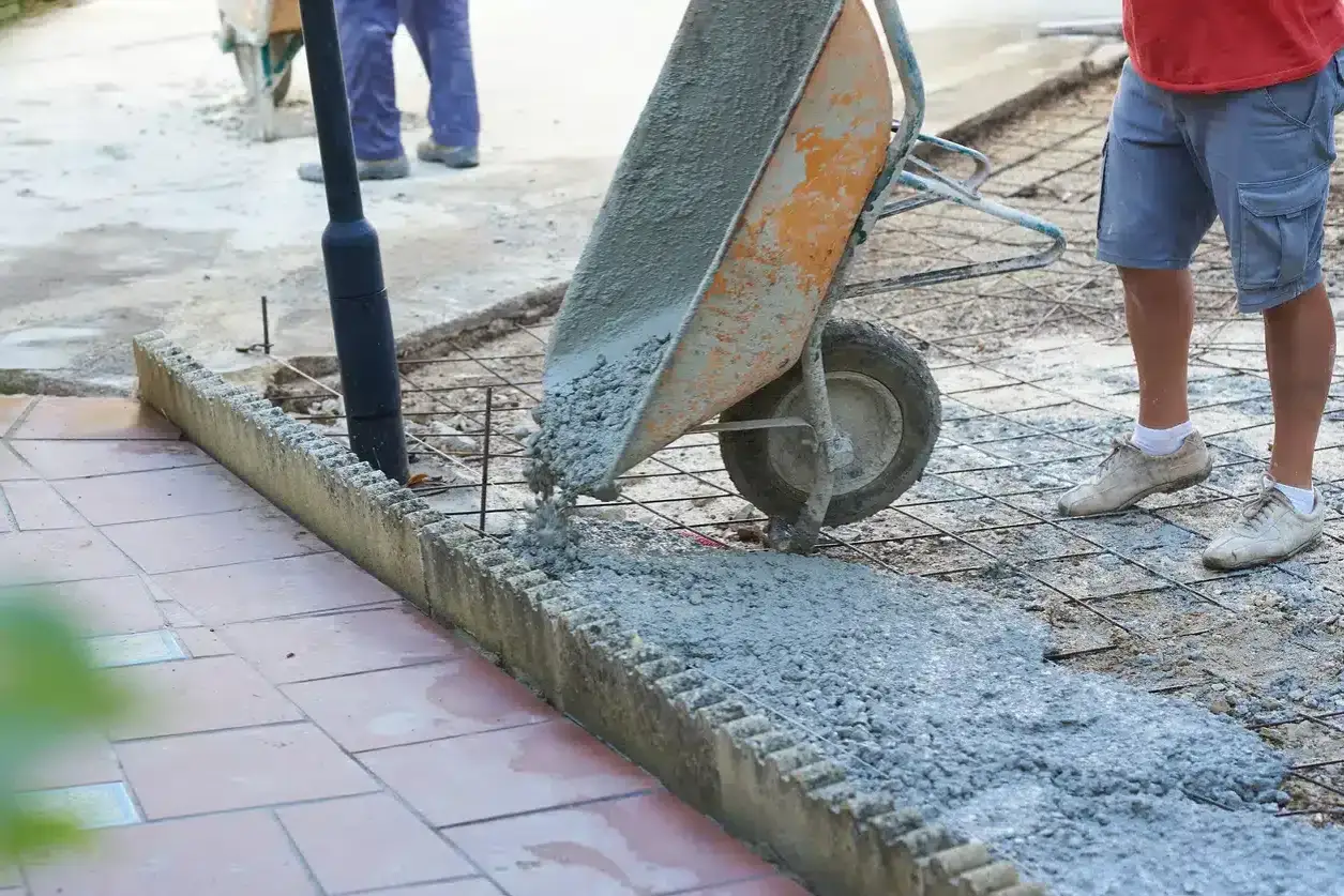Brouette déversant du béton frais sur une armature métallique. Matériaux pour terrasse béton en cours d'installation.