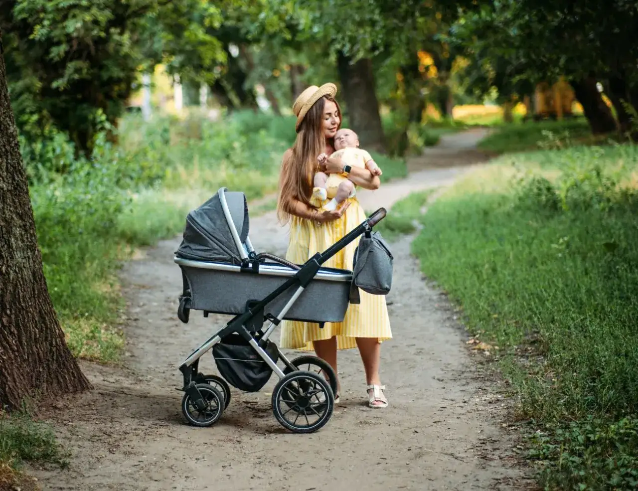 Mama z niemowlakiem w w&oacute;zku, planuje gdzie nad morze z niemowlakiem. Słoneczny dzień w parku.