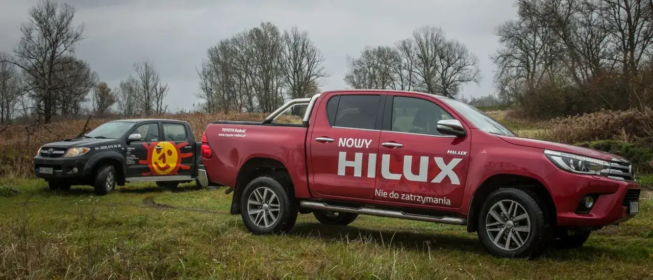 Dwa samochody terenowe Toyota Hilux, jeden czerwony z napisem 