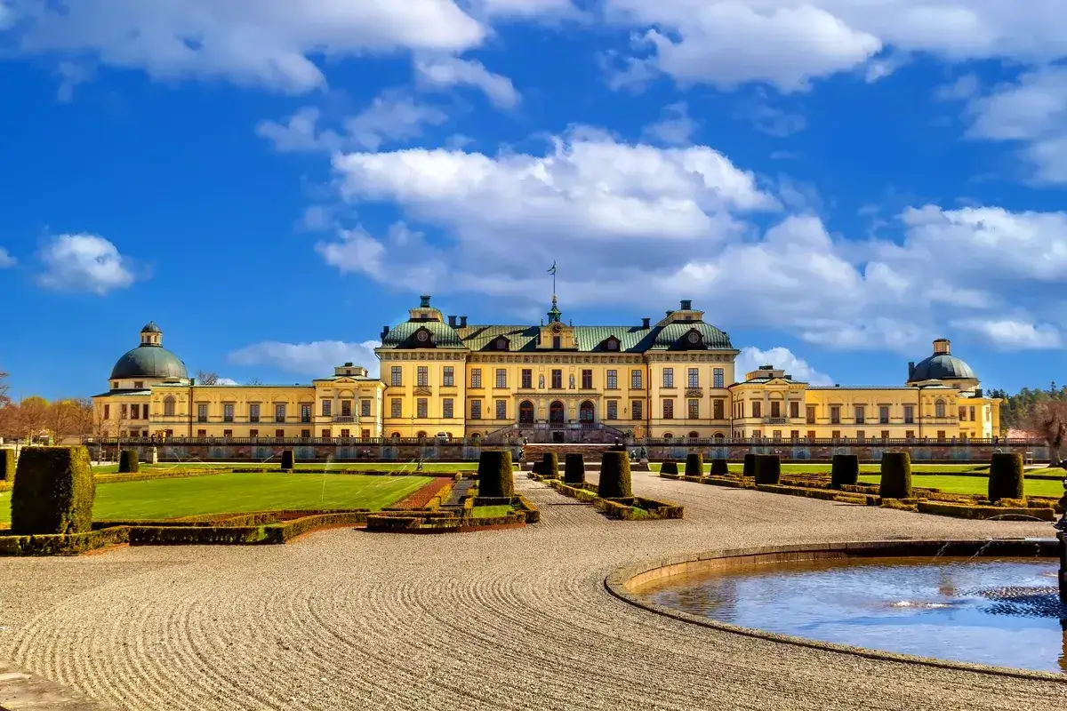Drottningholms slott, där kungen bor, med sina imponerande trädgårdar och kupoler under en blå himmel med moln.
