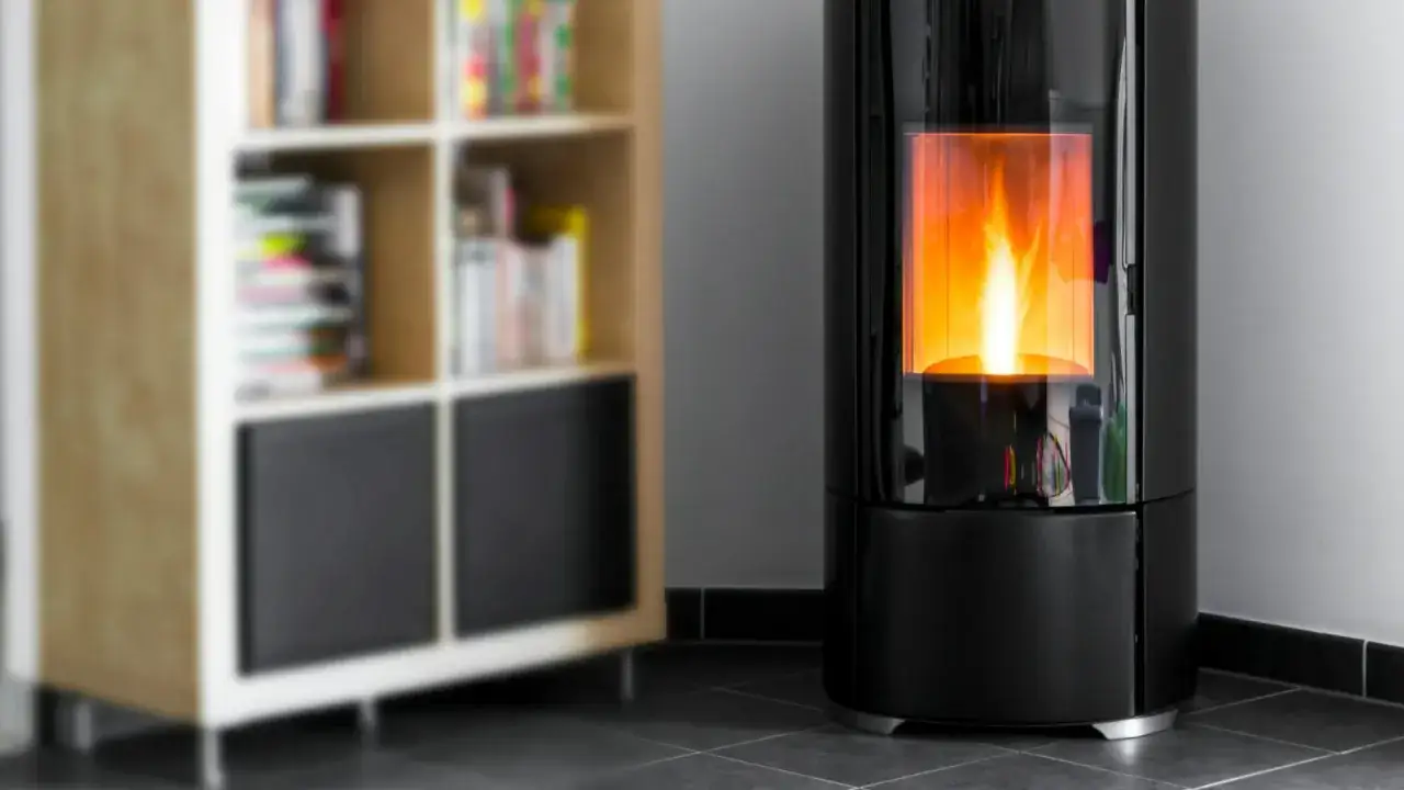 Un poêle à granulés noir moderne chauffe un appartement, avec une flamme vive visible à travers la vitre. Une bibliothèque floue se trouve à gauche.