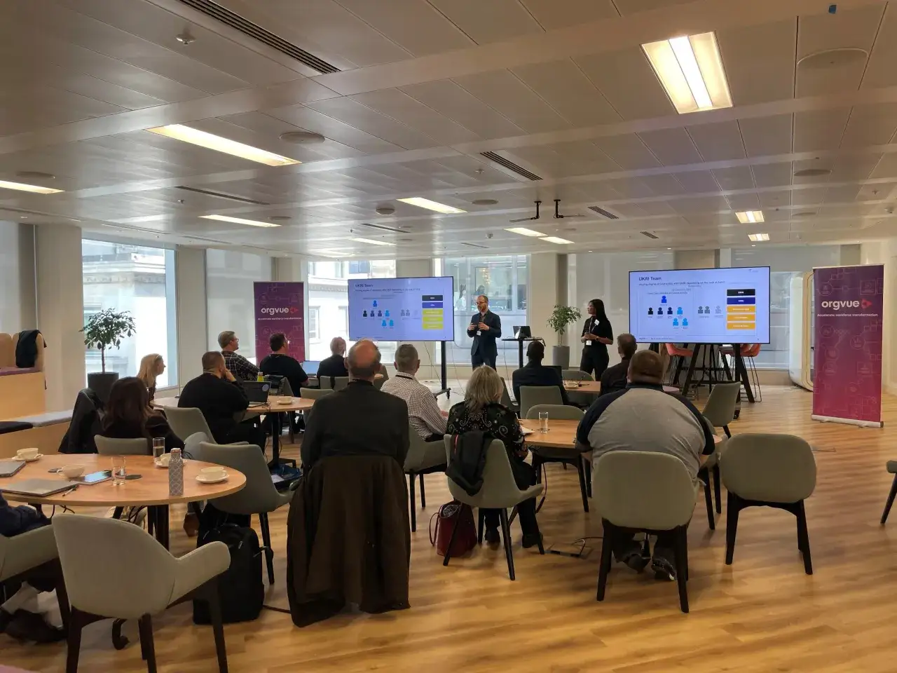 A presentation on workforce transformation, fostering external awareness, is underway in a modern office with attendees seated and listening.