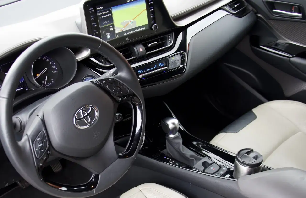 Wnętrze Toyoty C-HR 2019: kierownica, nawigacja, panel klimatyzacji i fotel pasażera.