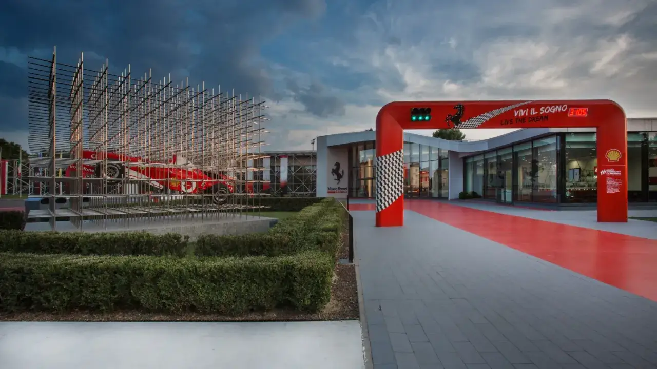 Muzeum Ferrari w Maranello. Czerwony bolid Formuły 1 w metalowej konstrukcji, wejście z bramką startową i hasłem