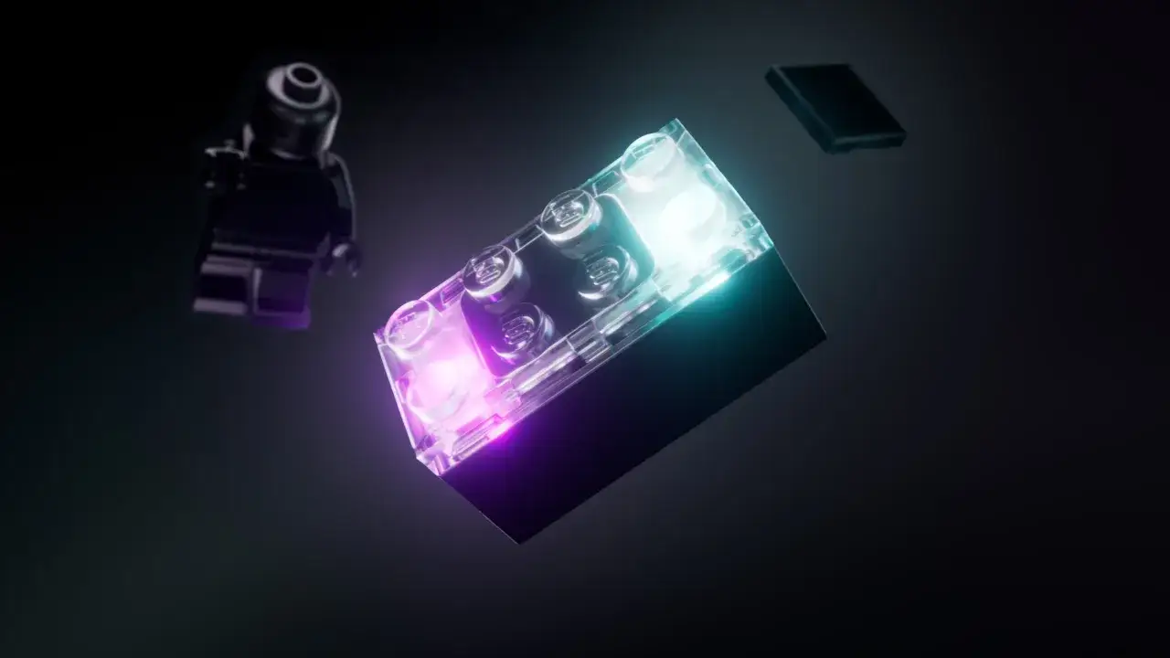 Ein leuchtender Lego Smart Brick in Lila und T&uuml;rkis schwebt neben einer schwarzen Lego-Figur und einem Smartphone.