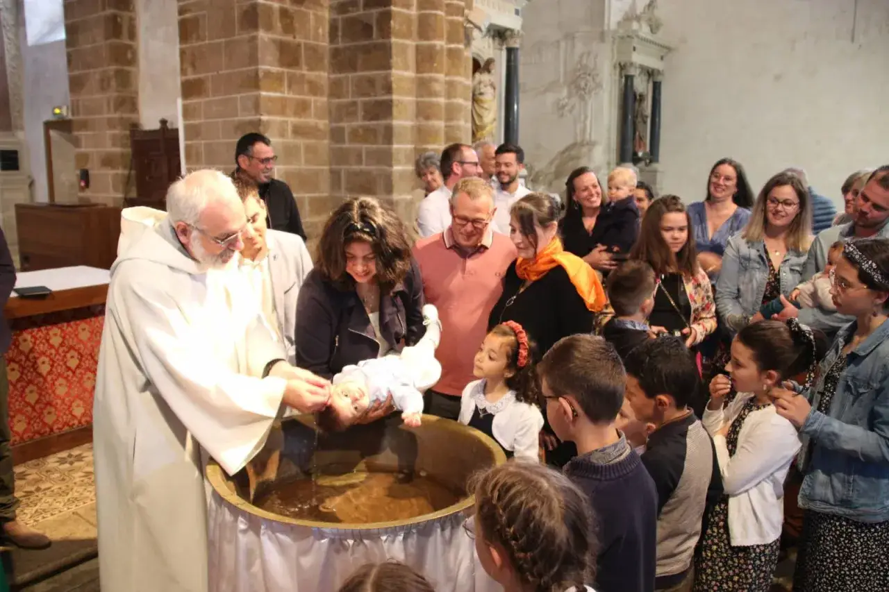 C&eacute;r&eacute;monie de messe bapteme dans une &eacute;glise. Un pr&ecirc;tre verse de l'eau sur un b&eacute;b&eacute; dans une cuve baptismale, entour&eacute; de sa famille et d'invit&eacute;s.