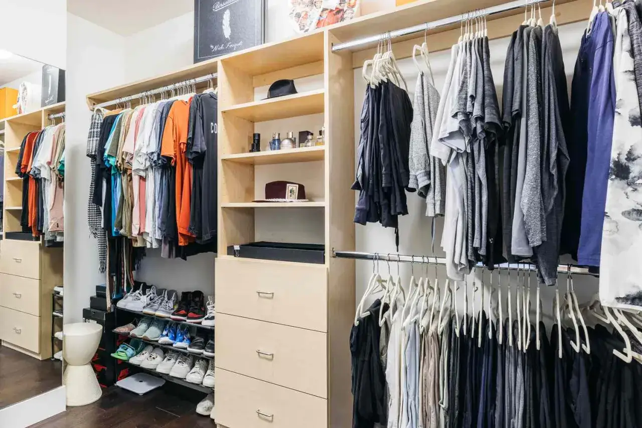 Interior de armario empotrado con ropa colgada y organizada, zapatos en estantes y cajones.