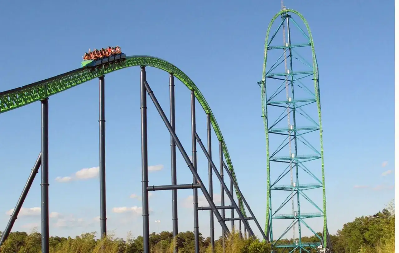 Wagonik z pasażerami pędzi po zielonej konstrukcji najwyższego rollercoastera na świecie, tuż przed pionowym spadkiem.