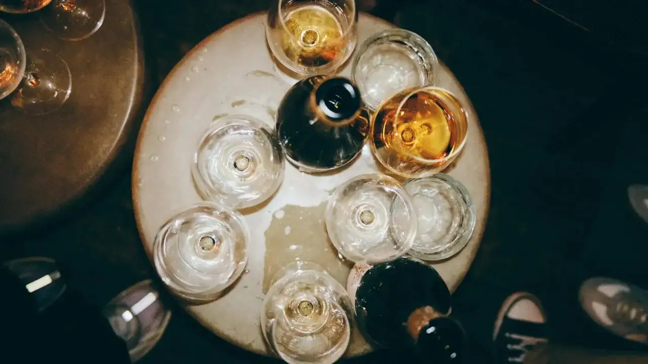 Degustacja różnych rodzajów win. Kieliszki z bursztynowym i bladym winem, butelki, wszystko na okrągłej tacy.