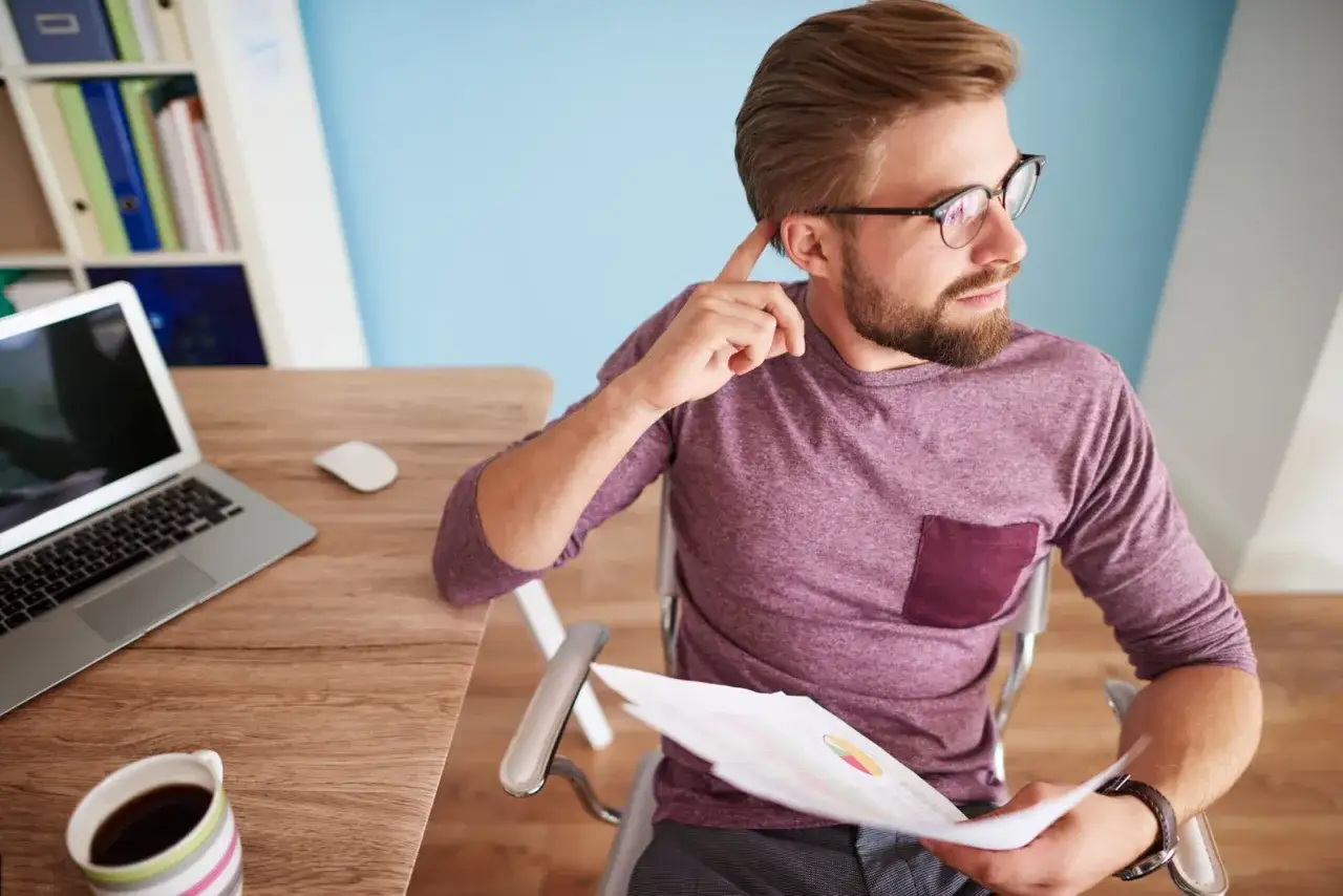 Hombre con gafas revisa gr&aacute;ficos, pensando si es un falso aut&oacute;nomo. Ejemplos de su situaci&oacute;n laboral se reflejan en su rostro.