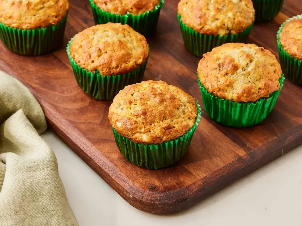 Kilka pysznych muffinek bananowych fit w zielonych papilotkach na drewnianej desce. Idealne na zdrową przekąskę.