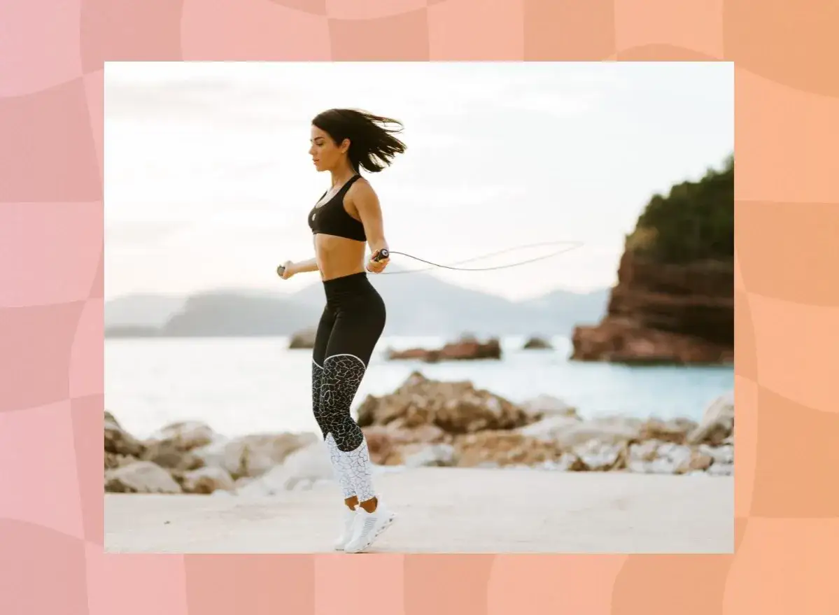 Femme en tenue de sport faisant de l'exercice corde &agrave; sauter sur une plage rocheuse, avec la mer et des falaises en arri&egrave;re-plan.