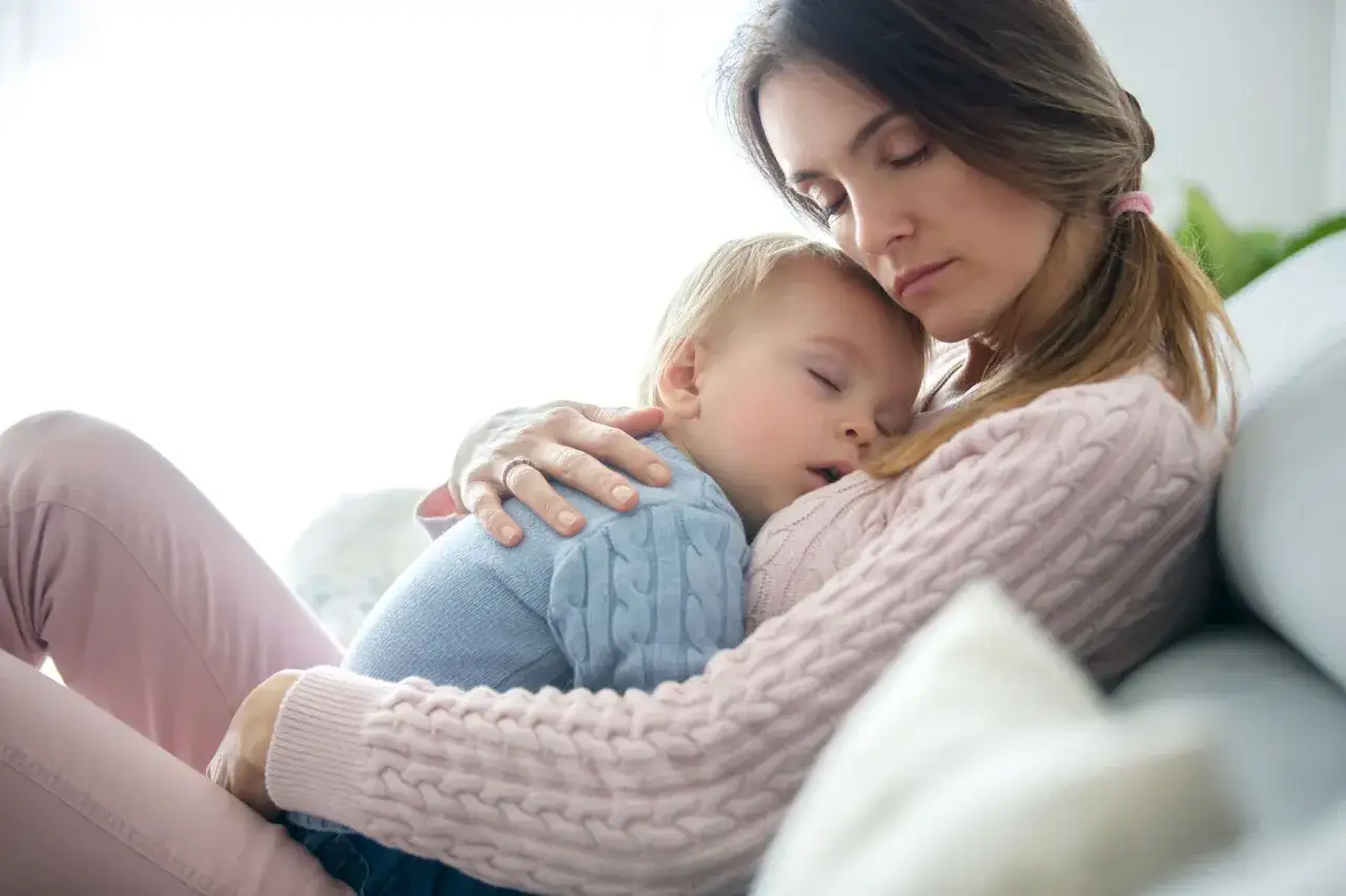 Matka tuli maleńkie dziecko do snu. Jej ręka obejmuje go, a na palcu widać obrączkę.