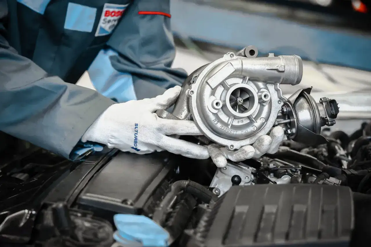 Mechanik w białych rękawiczkach trzyma turbosprężarkę, sprawdzając, jak sprawdzić czy turbina puszcza olej do intercoolera.
