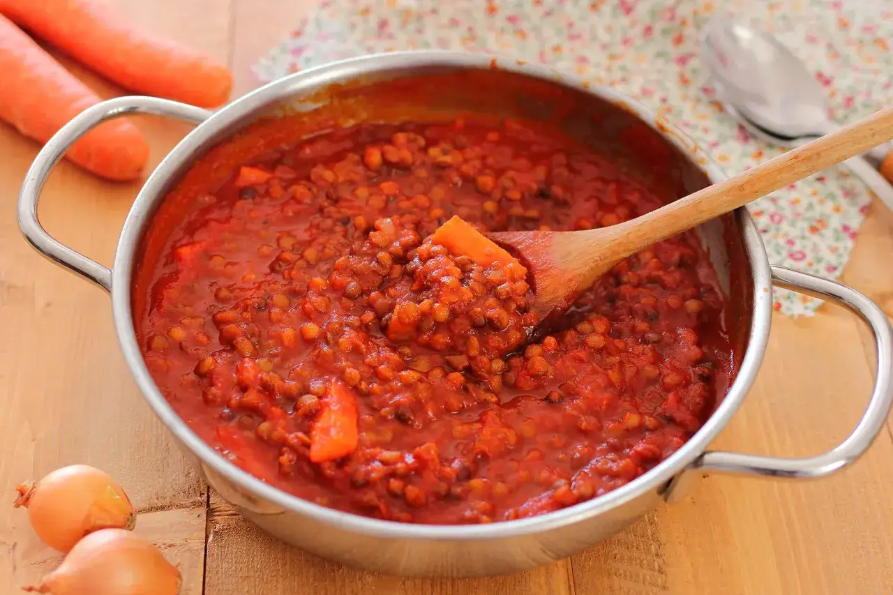 Un saporito ragù di lenticchie in una pentola, pronto per essere servito. Carote e cipolle sullo sfondo.