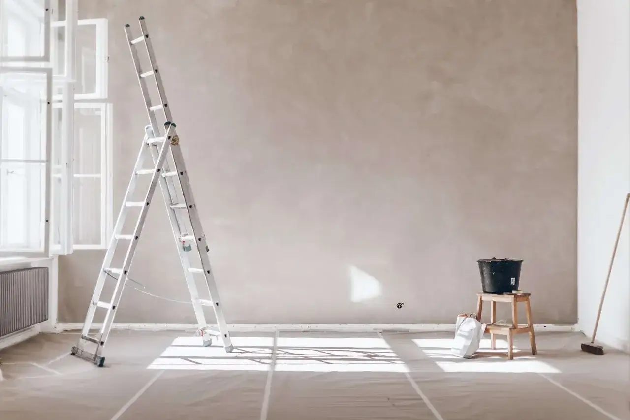 Stege och hink står redo för att blanda spackel med vatten. Rummet är förberett för renovering med skyddande plast på golvet.