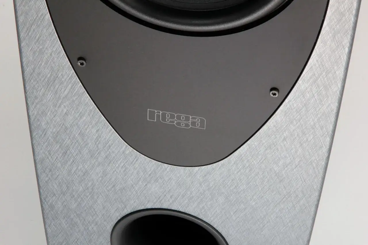 Gros plan sur une enceinte Rega, avec son logo gravé et une finition texturée argentée.